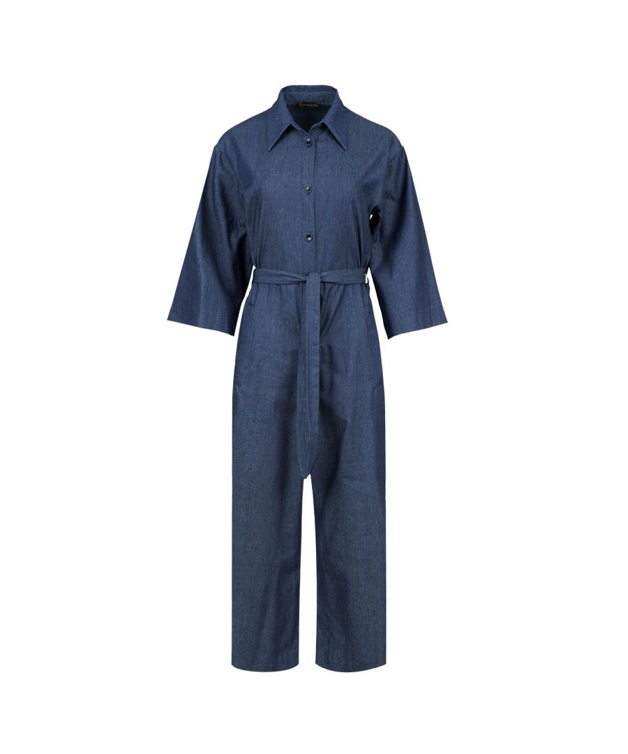 Deze indigo jumpsuit is gemaakt van katoen. Het heeft ¾ mouwen en een kraag. Er is een halssluiting met zwarte plastic knopen. Er zijn zakken aan de zijkanten met elk een riemlus. Het heeft een 3 cm brede ceintuur van dezelfde stof die door twee ceintuurlussen in de taille loopt. Aan de achterkant zit een omgekeerde plooi. De jumpsuit heeft een beenlengte van 7/8.