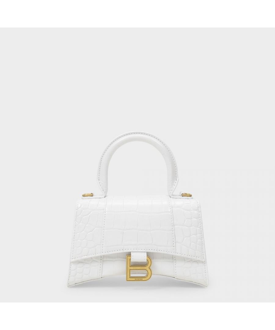 The mini Hourglass features the same curved, retro-futuristic vibe as its big brother. It comes in patent white croc-embossed leather this season, with a stiff top handle, a long flap, a magnetic clasp and a B in aged, silver-tone brass. A statement piece to wear with an all-black outfit, or a little lace dress. Top handle : 10 cm - Shoulder strap : 110 cm. Worn two ways - One top handle and One adjustable. detachable shoulder strap. Material : Croc-Embossed Calfskin. Lining : Leather. Colour : Blanc - 9016 White. Closure : Flap with Press Button. Interior : Patch pocket back.