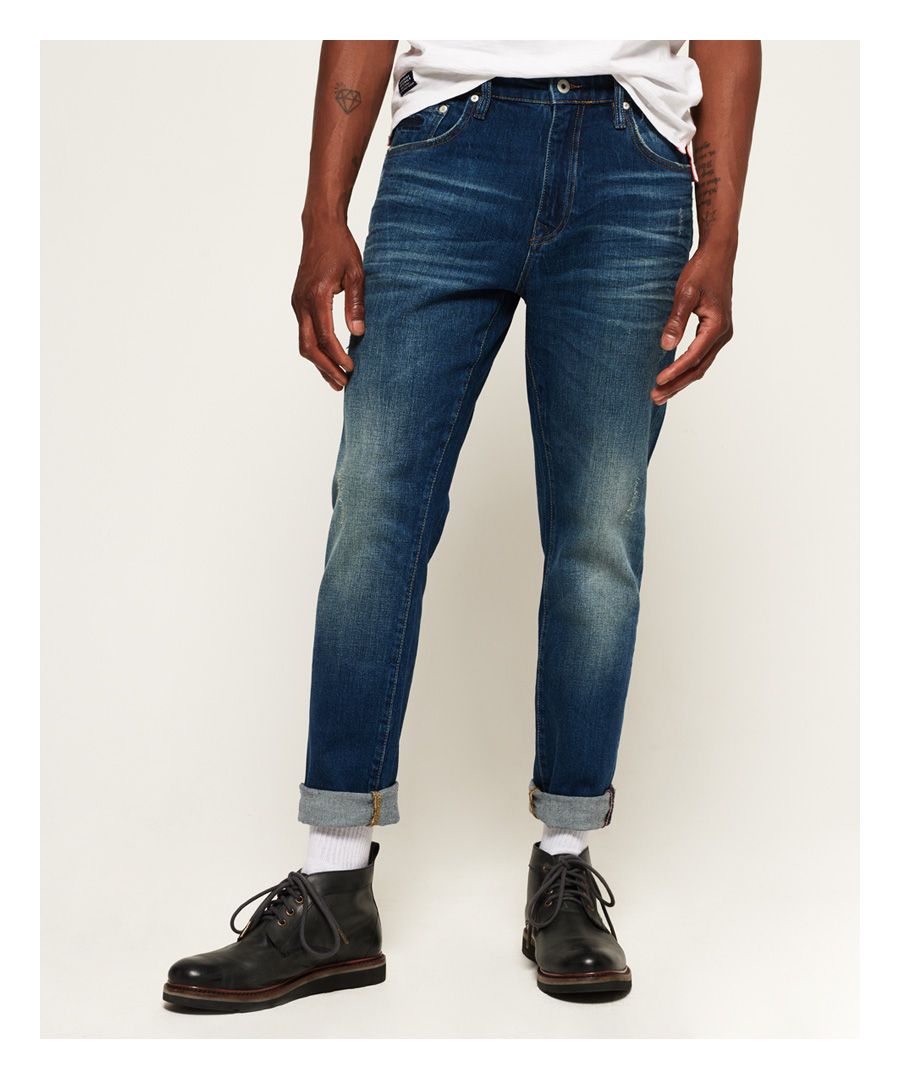 Superdry Conor-herenjeans met taps toelopende pijpen. De Conor-jeans is een goede keuze als je op zoek bent naar een jeans met ruimte rond de taille en het zitvlak in combinatie met taps toelopende broekspijpen. Met een ritssluiting, de klassieke vijf zakken en riemlussen. De Conor-jeans met taps toelopende pijpen heeft ook een geborduurde versie van het iconische Superdry-logo op het muntzakje, een leren logolabel op de tailleband en een Superdry-logolabel op een van de achterzakken.Taps toelopende pasvorm. Taps toelopende denim met ruimte op de dij, geleidelijk toelopend tot een slanke enkelopening, geeft een eigentijdse en meer op maat gemaakte look.