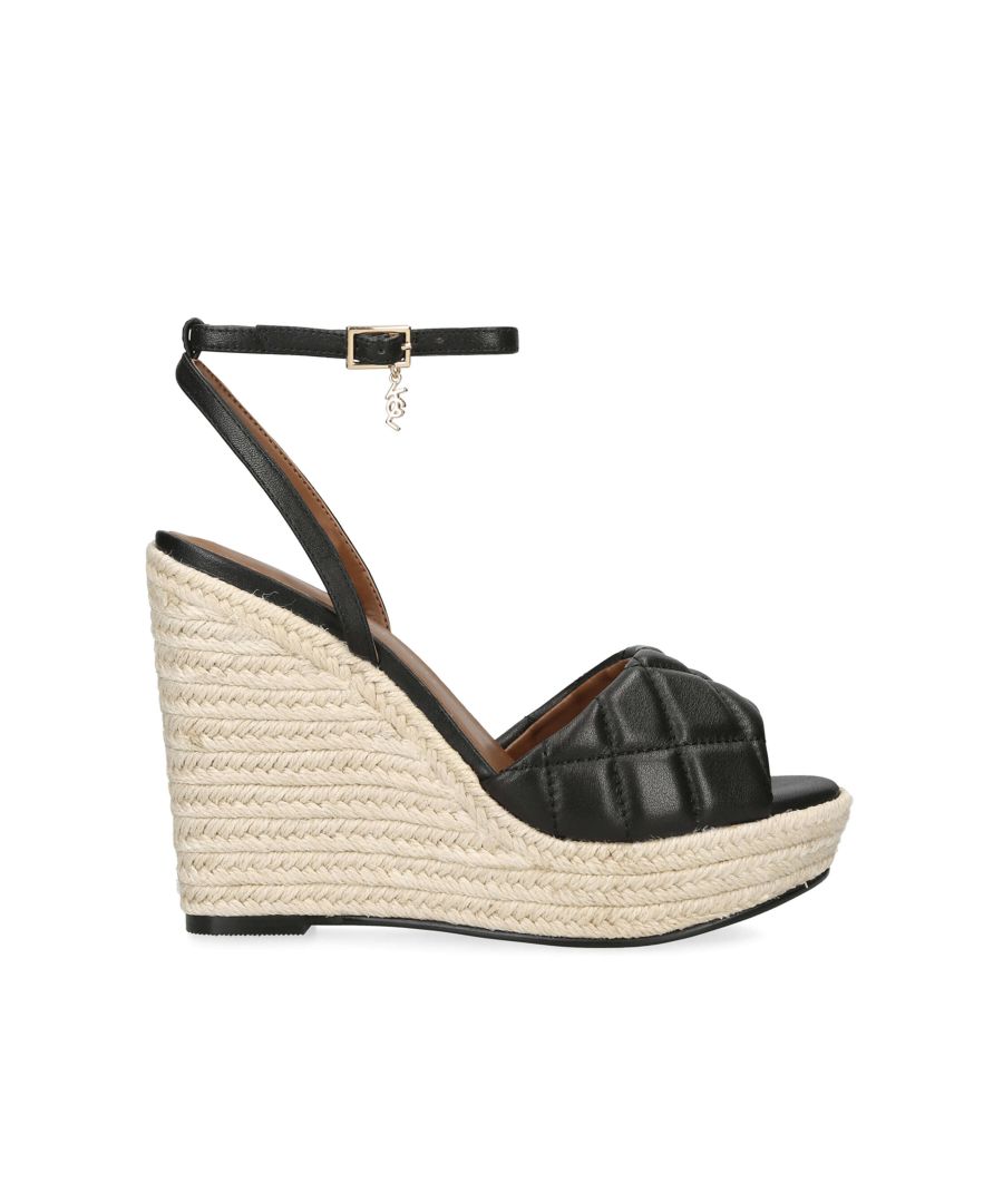 The Kurt Geiger London Brixton Wedge is a wedge heel. The upper is in a black leather with overstitch quilt across the toe strap. There is a small gold tone KGL charm on the buckle. The wedge heel sits at 10.5cm.