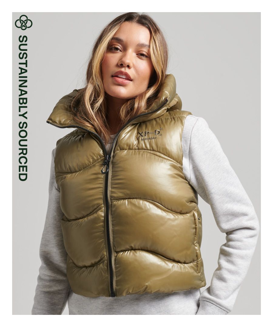 Het korte model van de glanzende gewatteerde bodywarmer geeft je laagjesoutfit een elegante touch, terwijl de luxe combinatie van een zachte voering en gewatteerde vulling voor voldoende warmte zorgt. Dankzij het klassieke mouwloze ontwerp kun je actief zijn en heb je maximale bewegingsvrijheid. Ook is hij lichtgewicht, wat deze bodywarmer een uitstekende keuze maakt die zowel functioneel als behaaglijk is.Gewatteerd ontwerpCapuchon met verstelbaar trekkoordRitssluitingGeborduurde details op de borstTwee zijzakken met ritsVerstelbaar elastisch trekkoord in de zoomVolledig gevoerdDe wattering in deze jas is gemaakt van 100% gerecycled materiaal. Elke jas bevat tot 20 gerecyclede flessen, waardoor wordt voorkomen dat deze flessen op een vuilnisbelt terechtkomen of onze oceanen vervuilen.