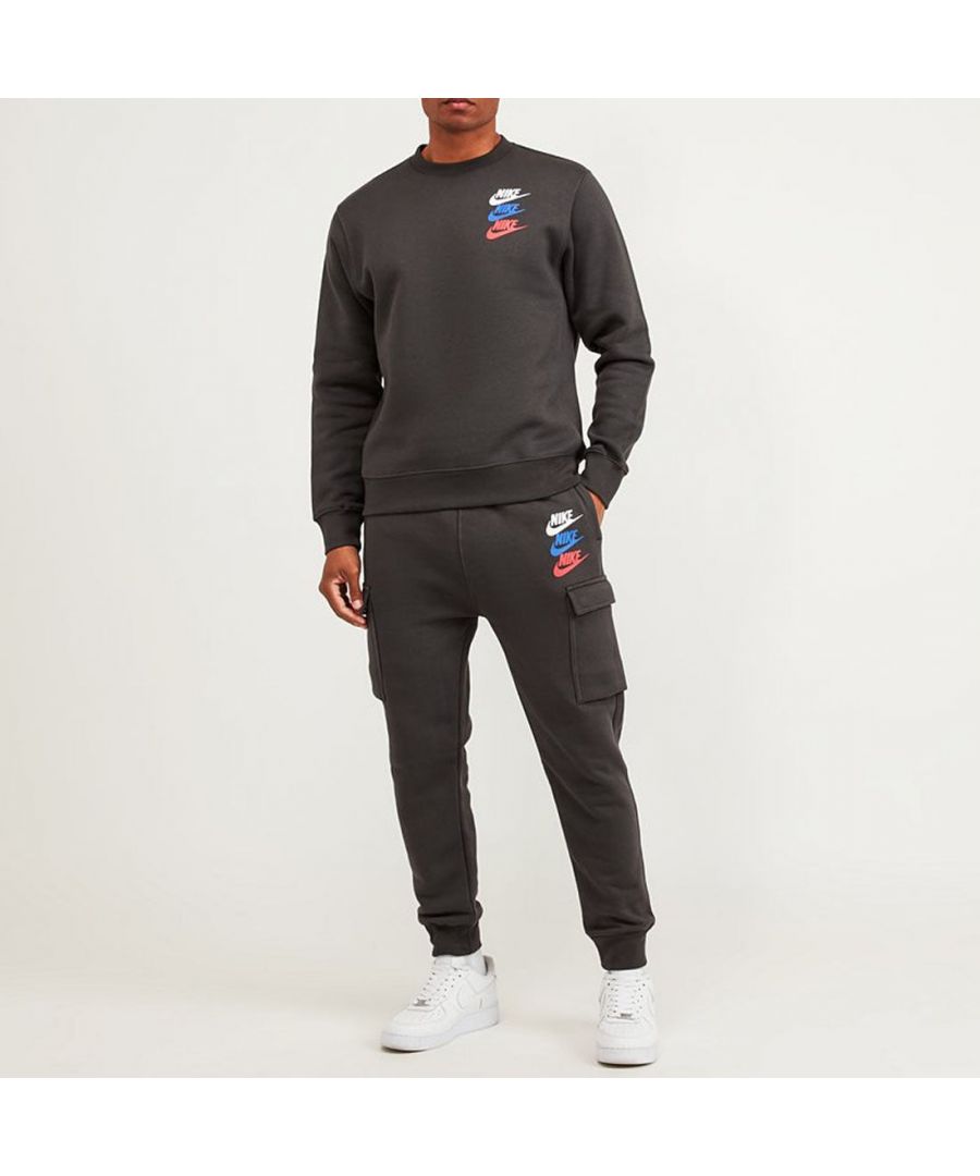 Nike Standard Issue Fleece Tracksuit in Dark Smoke Grey. Bags and bags of style on display here, but not at the expense of comfort. Crafted from soft cotton-rich fleece fabric into a highly functional and sporty aesthetic. The material is slightly brushed to the back for superior softness. With an elasticated adjustable drawstring waistband, jogger-inspired rib cuffs, hand pockets, cargo leg pockets and 1990’s-inspired screen printing for a street ready look.