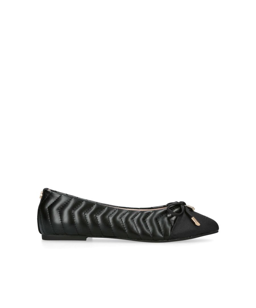 The Lily Ballerina flat shoe features a black exterior with overstitch chevron quilt. There is a gold padlock charm on the bow. The back of the ankle features a micro gold tone Icon C.